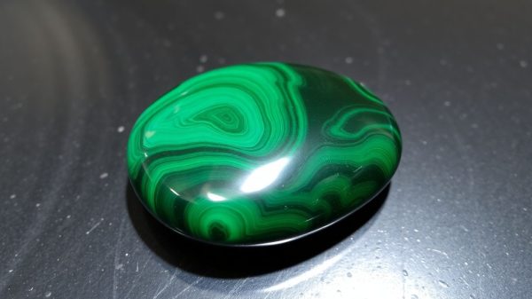 Polished malachite stone with green banding on dark surface.