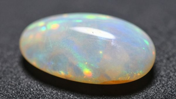 Polished opal with iridescent play-of-color on dark surface.