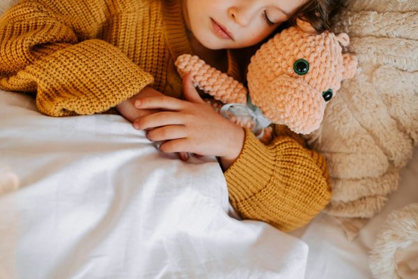 Sleeping child hugging a soft teddy bear in bed, used to illustrate soothing bedtime restlessness in children.