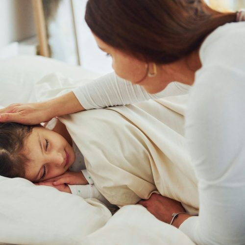 Parent gently soothing child in bed to ease bedtime resistance in children.
