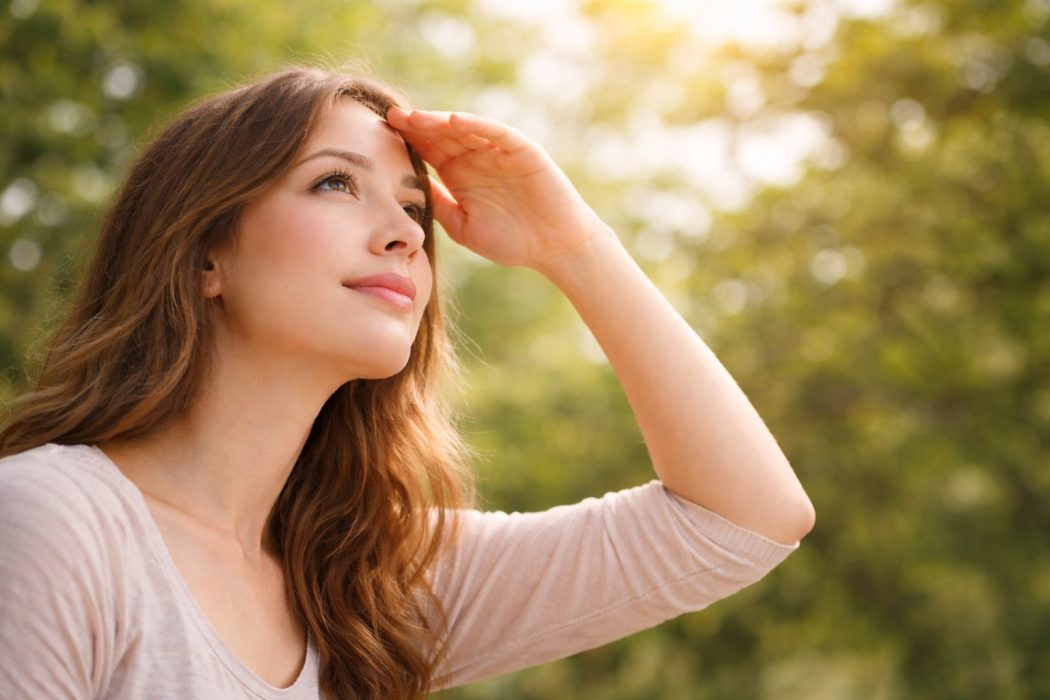 Woman shielding her eyes from sunlight while looking into the distance, reflecting floaters in your vision and liver health in TCM